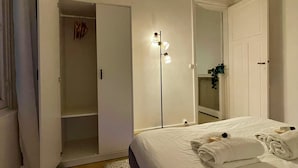 Een slaapkamer met een bed, een garderobe, een spiegel en een vloerlamp.