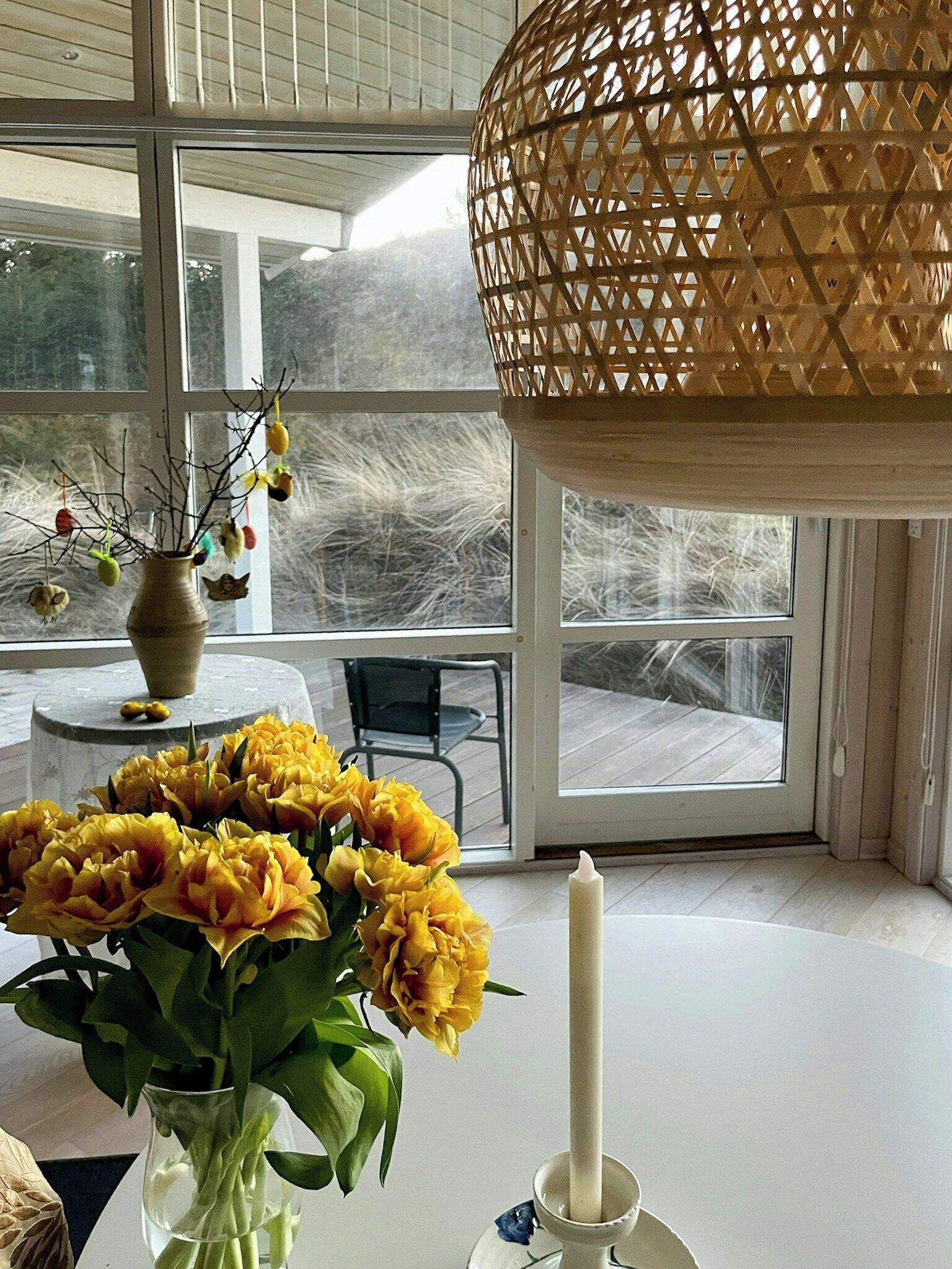 Une pièce dotée d’une grande fenêtre, d’une table ornée d’un vase de fleurs et d’un luminaire suspendu.