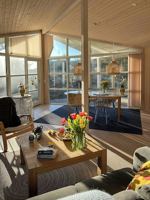A spacious living room with a large window, a dining area, and a cozy seating arrangement. - House with wide views in dunes near Blokhus (Blokhus)