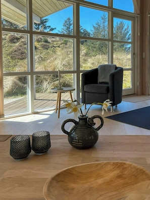 A room with large windows, a chair, a table with a vase and candle holders, and a wooden floor. - House with wide views in dunes near Blokhus (Blokhus)