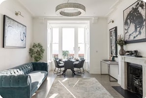 A modern living room with a sofa, dining table, and chairs, a fireplace, and artwork on the walls. - 3 bedroom, 3 bathroom ocean view with padel boards (Hastings)