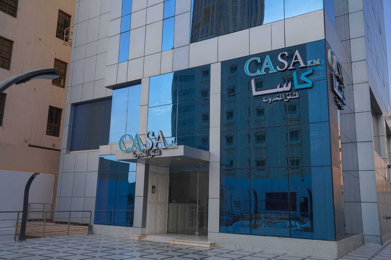 A modern building with the sign 'CASA' prominently displayed, featuring a reflective glass facade and a tiled entrance area.
