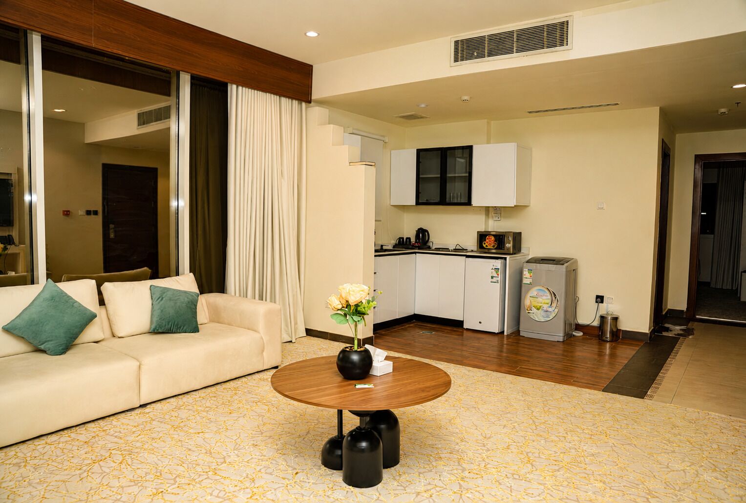 A modern living room with a sofa, a coffee table, and a kitchen area with a refrigerator and microwave.