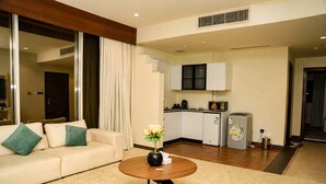 A modern living room with a sofa, a coffee table, and a kitchen area with a refrigerator and microwave.