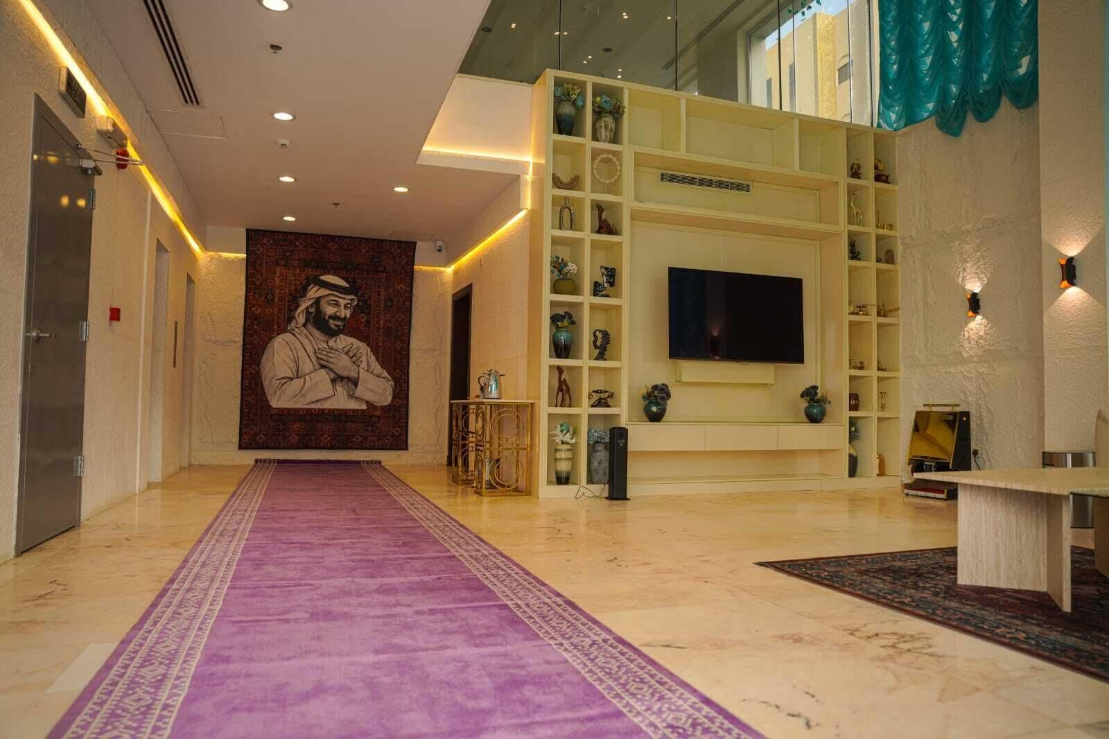 A hotel lobby with a purple carpet, a large wall mural, a TV, and shelves with decorative items.