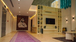 A hotel lobby with a purple carpet, a large wall mural, a TV, and shelves with decorative items.