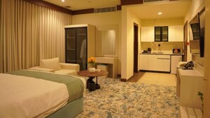 A hotel room with a bed, a seating area, a small table with a vase, and a kitchenette.