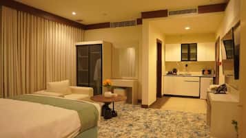 A hotel room with a bed, a seating area, a small table with a vase, and a kitchenette.