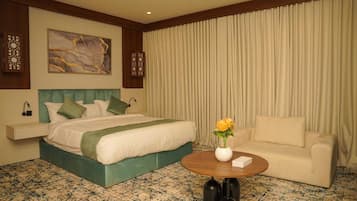 A hotel room with a bed, a sofa, a coffee table with a vase of flowers, and a wall with a painting.