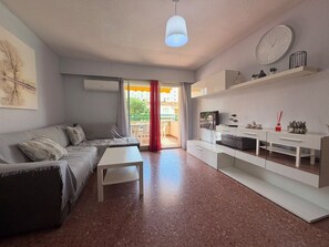 Ein modernes Wohnzimmer mit einer Couch, einem Couchtisch, einem Fernseher und einer Küchenzeile inklusive Kühlschrank und Mikrowelle.