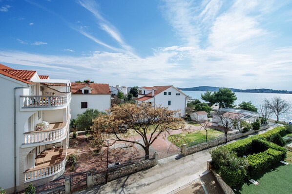 Una zona residenziale sul lungomare, con edifici a tetto di tegole rosse, un balcone con mobili da esterno e vista mare.