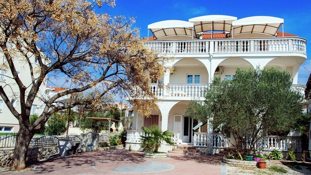 A multi-story building with balconies, a courtyard with a palm tree, and a stone wall. - Moretti Stay Near Vodice Center (Vodice)