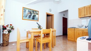 A dining area with a wooden table and chairs, a vase with flowers, a framed picture on the wall, and a kitchen in the background. - Moretti Stay Near Vodice Center (Vodice)