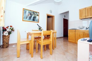 Ein Essbereich mit Holztisch und Stühlen, einer Blumenvase, einem gerahmten Bild an der Wand und einer Küche im Hintergrund.
