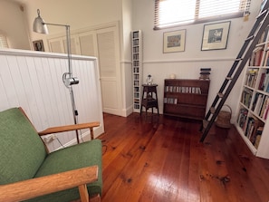 A room with a green chair, a floor lamp, a bookshelf, a ladder, and a radiator.