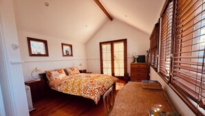 Une chambre à coucher comprenant un lit, une commode, un bureau et une fenêtre avec des stores.