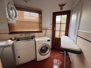 A compact laundry room with a washing machine, a dryer, a sink, and a window with blinds.