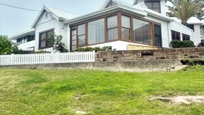 Une maison moderne à deux étages, dotée de grandes fenêtres, d’un mur de soutènement en pierre et d’une clôture blanche en bois.