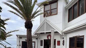 Una casa blanca con terraza de madera, una palmera y vista al océano.