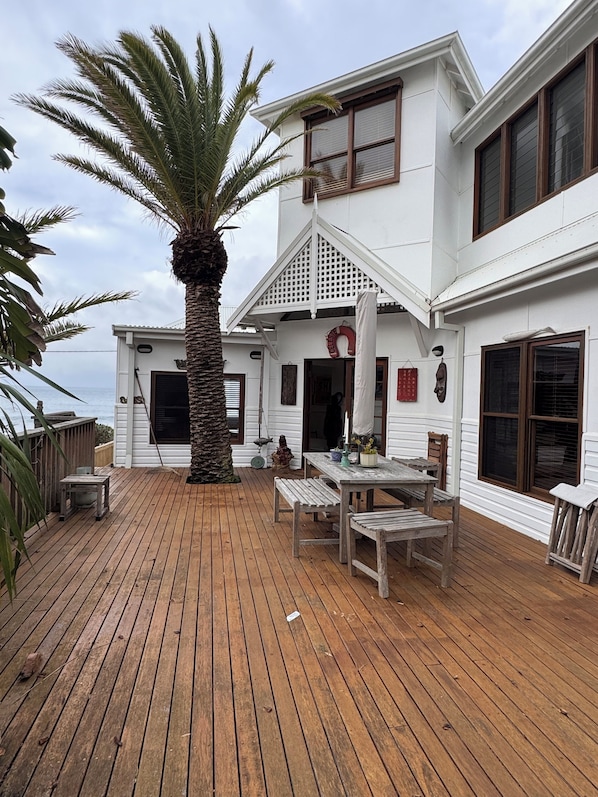 A white house with a wooden deck, a palm tree, and a view of the ocean.