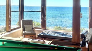 Une table de billard placée devant de grandes fenêtres offrant une vue sur la mer.
