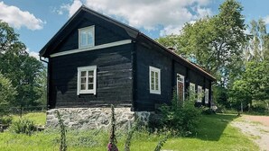 Une maison en bois, avec des fondations en pierre, entourée de verdure et de fleurs.