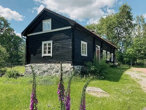 A wooden house with a stone foundation, surrounded by greenery and flowers. - Historic 19th century cottage in Blekinge (Kyrkhult)