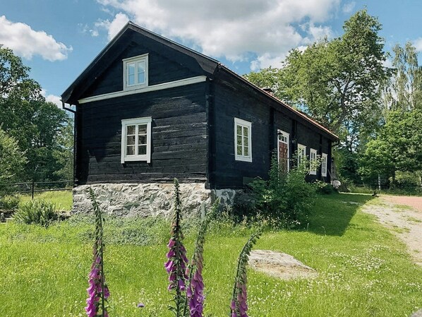 Une maison en bois, avec des fondations en pierre, entourée de verdure et de fleurs.