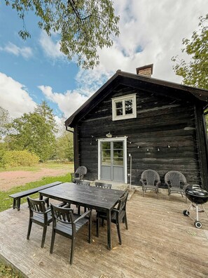 Une cabane en bois avec une terrasse, une table et des chaises, et un barbecue.