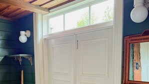 Une porte à deux battants, de couleur blanche, avec une poignée en laiton, un plafond en bois et une petite fenêtre au-dessus.