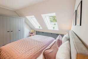 A bedroom with a sloped ceiling, skylights, a bed with a pink quilt, and grey storage units. - Romantic countryside in East Frisia (Friedeburg)