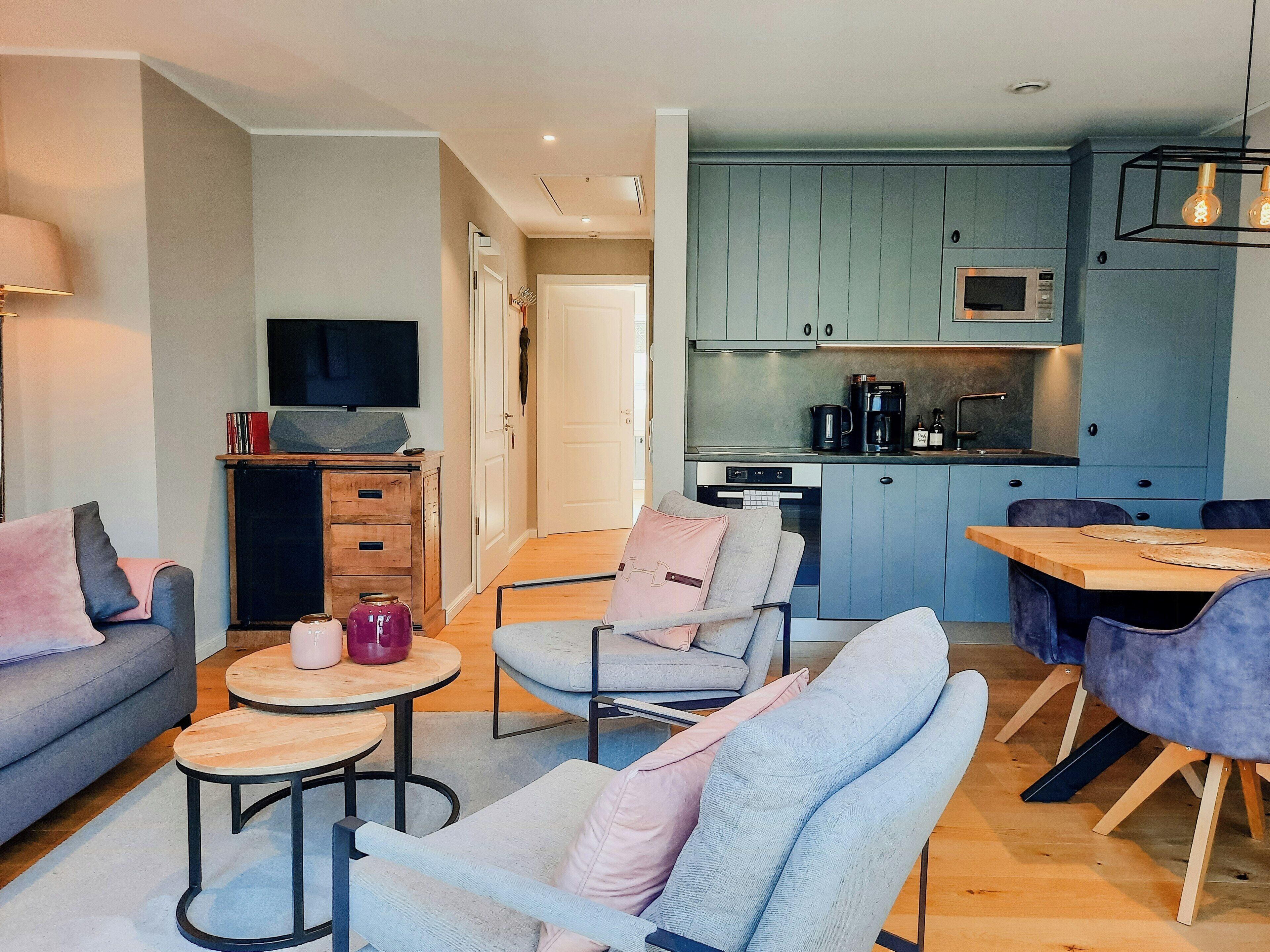 Ein modernes Wohnzimmer mit einer Couch, Sesseln, einem Couchtisch und einem Fernseher.