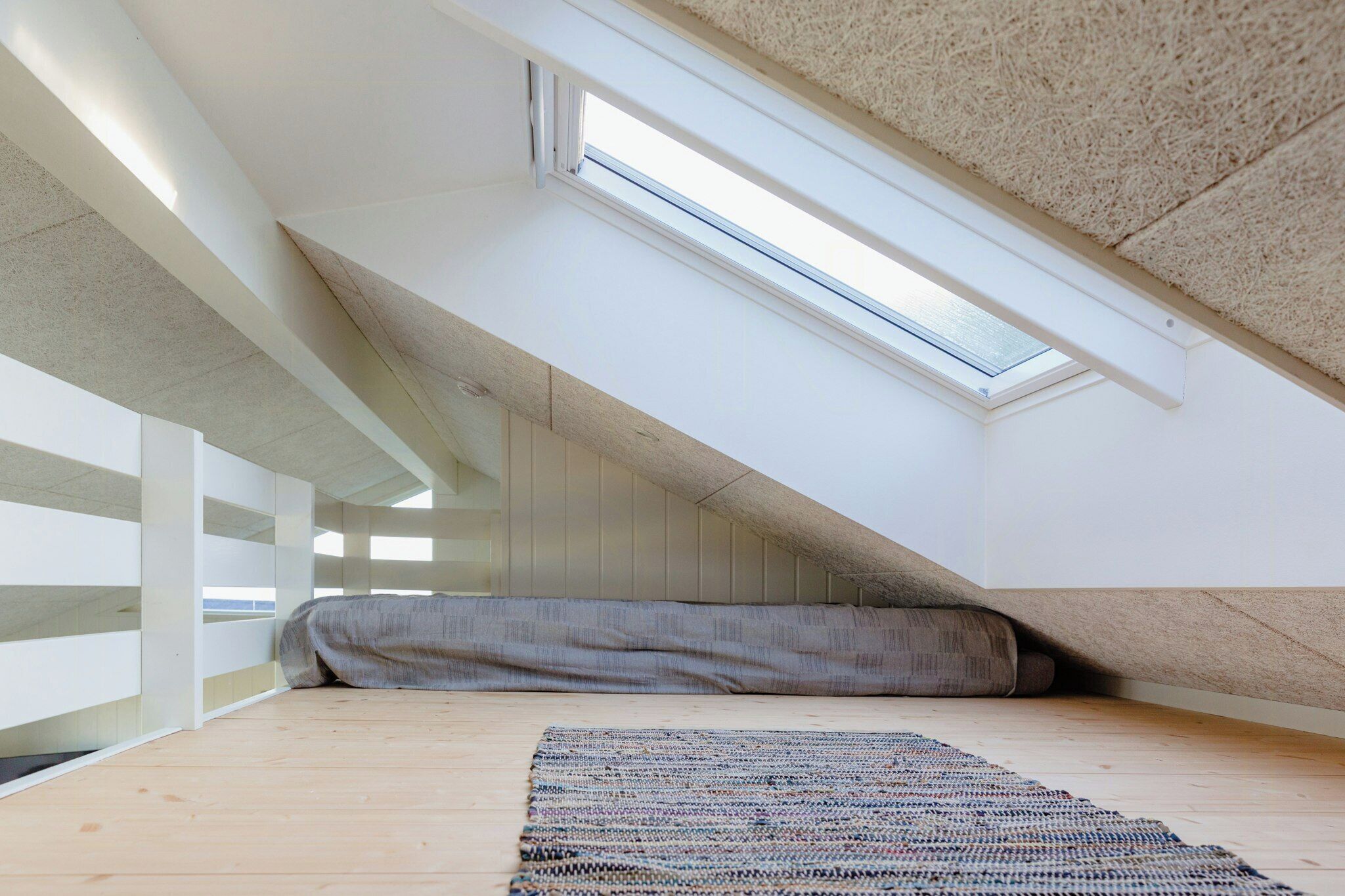 A sloped ceiling with a skylight, a wooden floor, and a patterned rug.