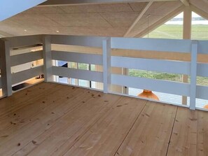 Ein Zimmer mit Holzboden, weißen Wänden und einem großen Fenster mit Blick ins Freie.