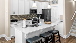 A kitchen with white cabinets, stainless steel appliances, a marble countertop, and two bar stools. - Saltlife - Beachside Townhome - Pool - Just Steps from Beach (Mexico Beach)