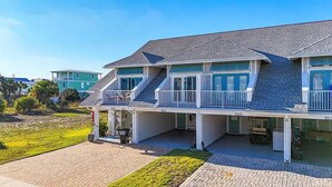 A two-story house with a covered porch, a garage, and a well-maintained lawn. - Saltlife - Beachside Townhome - Pool - Just Steps from Beach (Mexico Beach)
