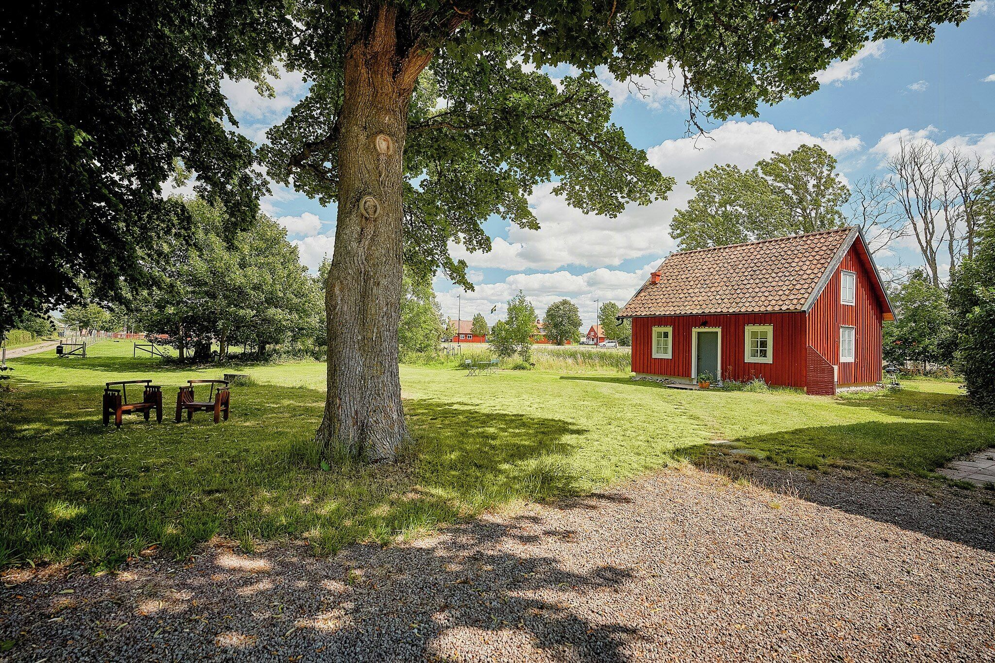 Un bâtiment en bois rouge avec une porte verte, entouré d’une zone herbeuse et d’arbres.