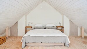 A bedroom with a sloped ceiling, a bed with a white and striped bedspread, two bedside tables with lamps, and a wooden floor. - Charming Hen House with Terrace near Vadstena (Vadstena)