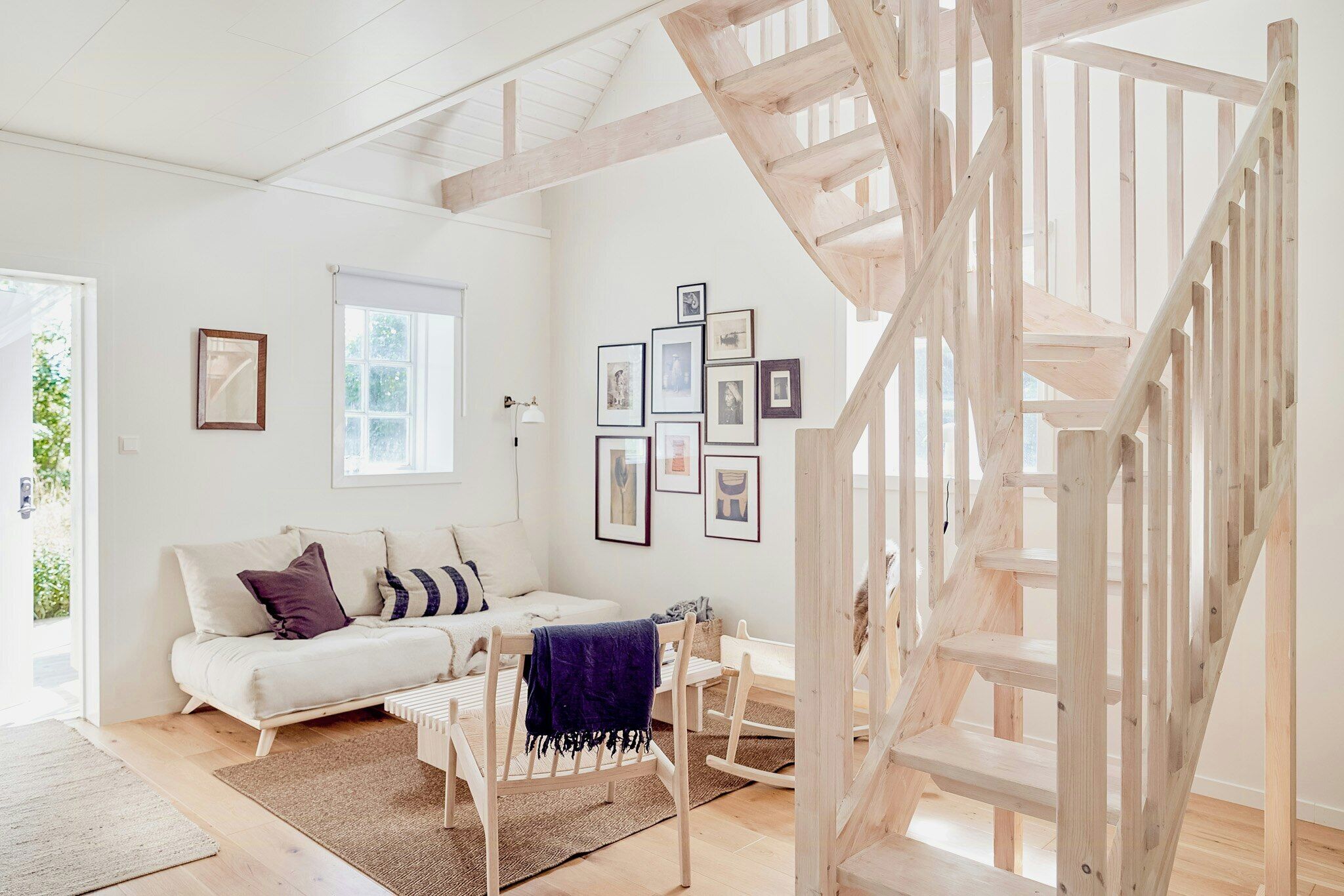 Ein Zimmer mit einer Holztreppe, einem weißen Sofa, einem kleinen Tisch und gerahmten Bildern an der Wand.