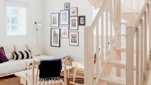 A spacious living room with a wooden staircase, a white sofa, a coffee table, and a wall adorned with framed pictures. - Charming Hen House with Terrace near Vadstena (Vadstena)