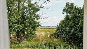 A view through a doorway with a wooden table and chairs, surrounded by lush greenery and a field in the distance. - Charming Hen House with Terrace near Vadstena (Vadstena)