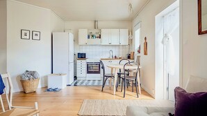 A modern kitchen with white cabinets, a dining area with a table and chairs, and a living room with a sofa and a purple cushion. - Charming Hen House with Terrace near Vadstena (Vadstena)