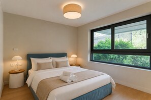 A bedroom with a bed, bedside lamps, a window, and a view of greenery. - Luxury Athenian Riviera Villa with Private Pool (Vouliagmeni)
