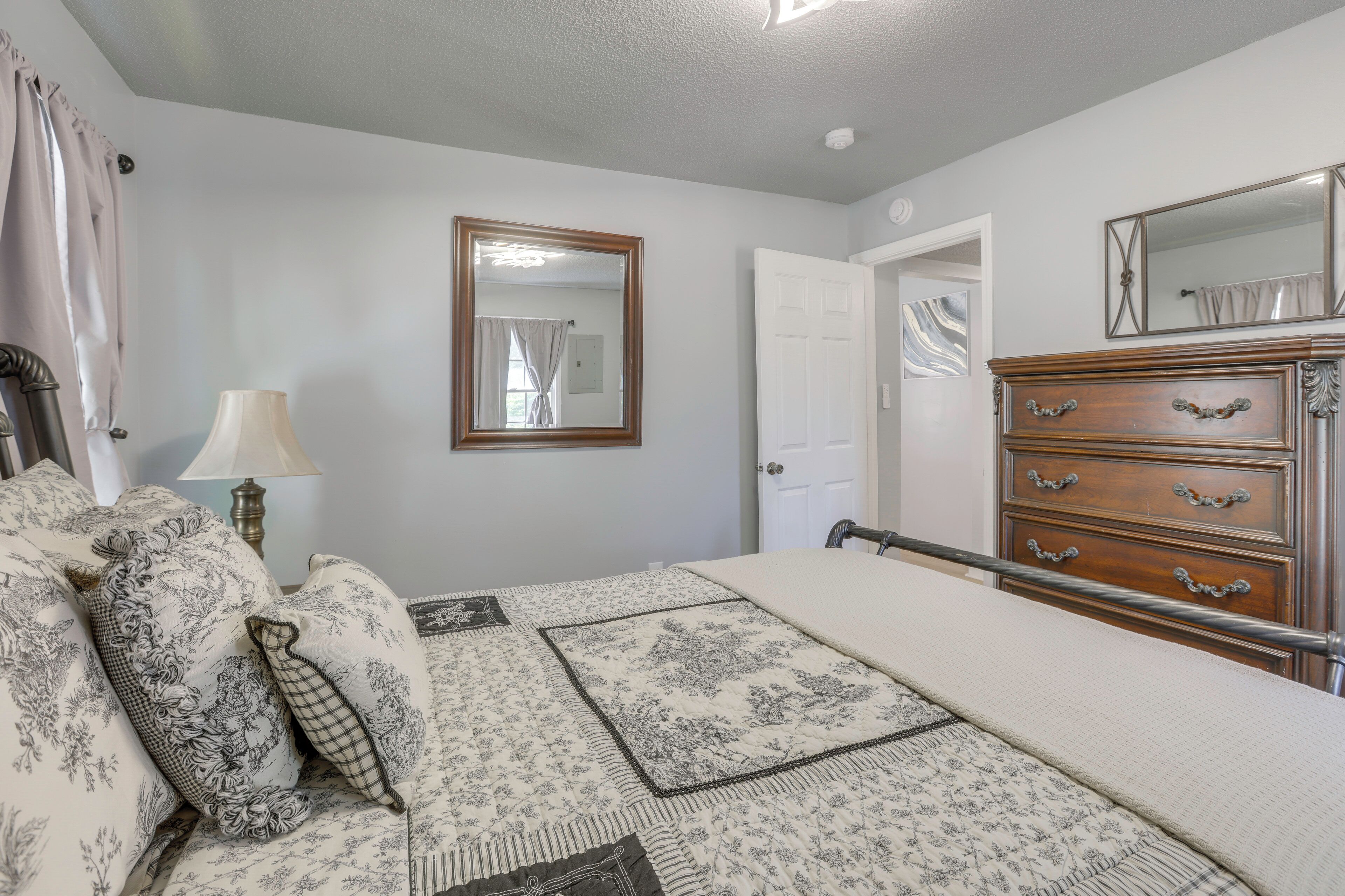 A bedroom with a bed, dresser, mirror, and a door leading to another room.