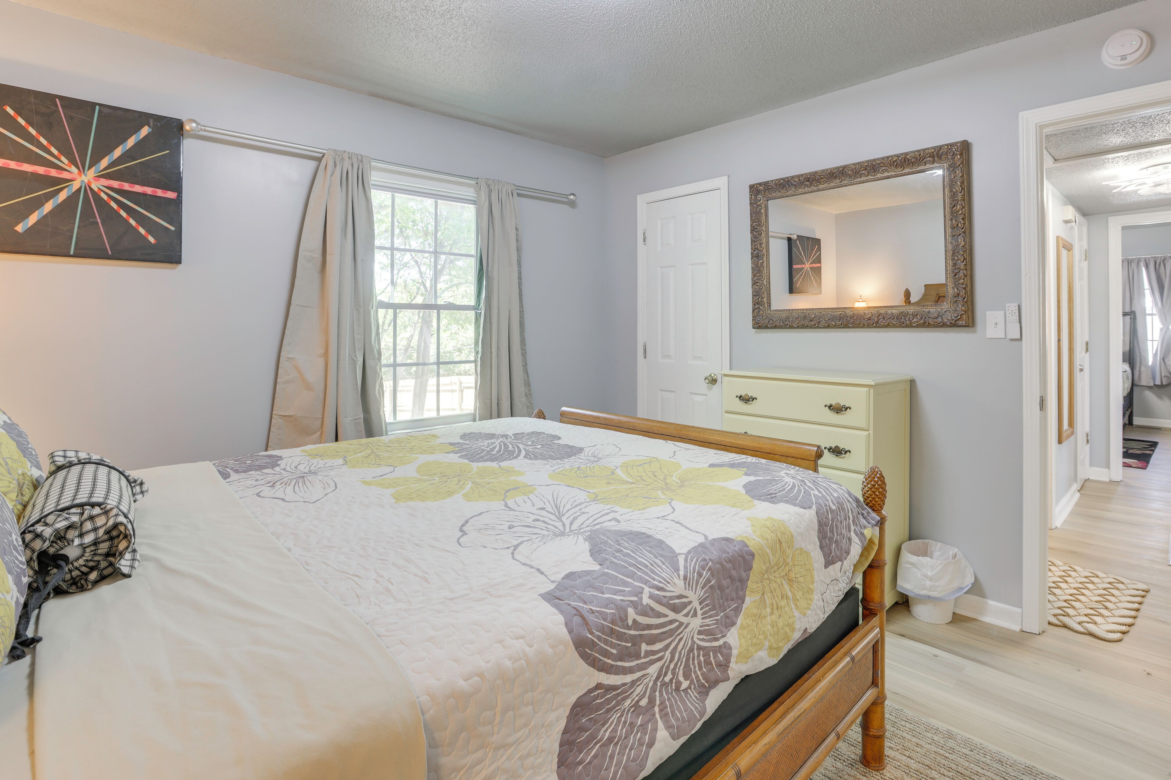 Un dormitorio con cama, cómoda, espejo y puerta que da a otra habitación.