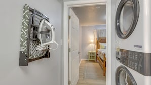 A laundry room with a wall-mounted dryer, a washing machine, and a door leading to a bedroom with a bed and a nightstand. - Renovated Birmingham Cottage: Great Outdoor Space! (Birmingham)