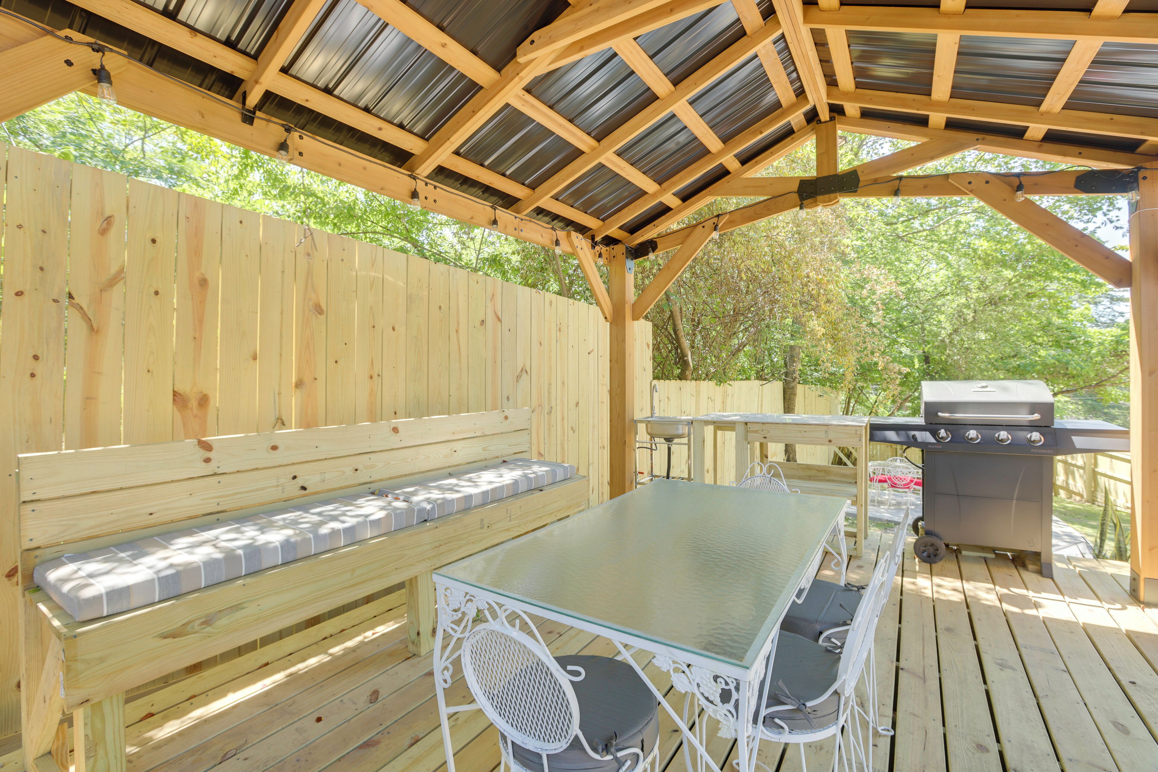 A covered outdoor patio with a wooden bench, a glass table, metal chairs, and a barbecue grill.