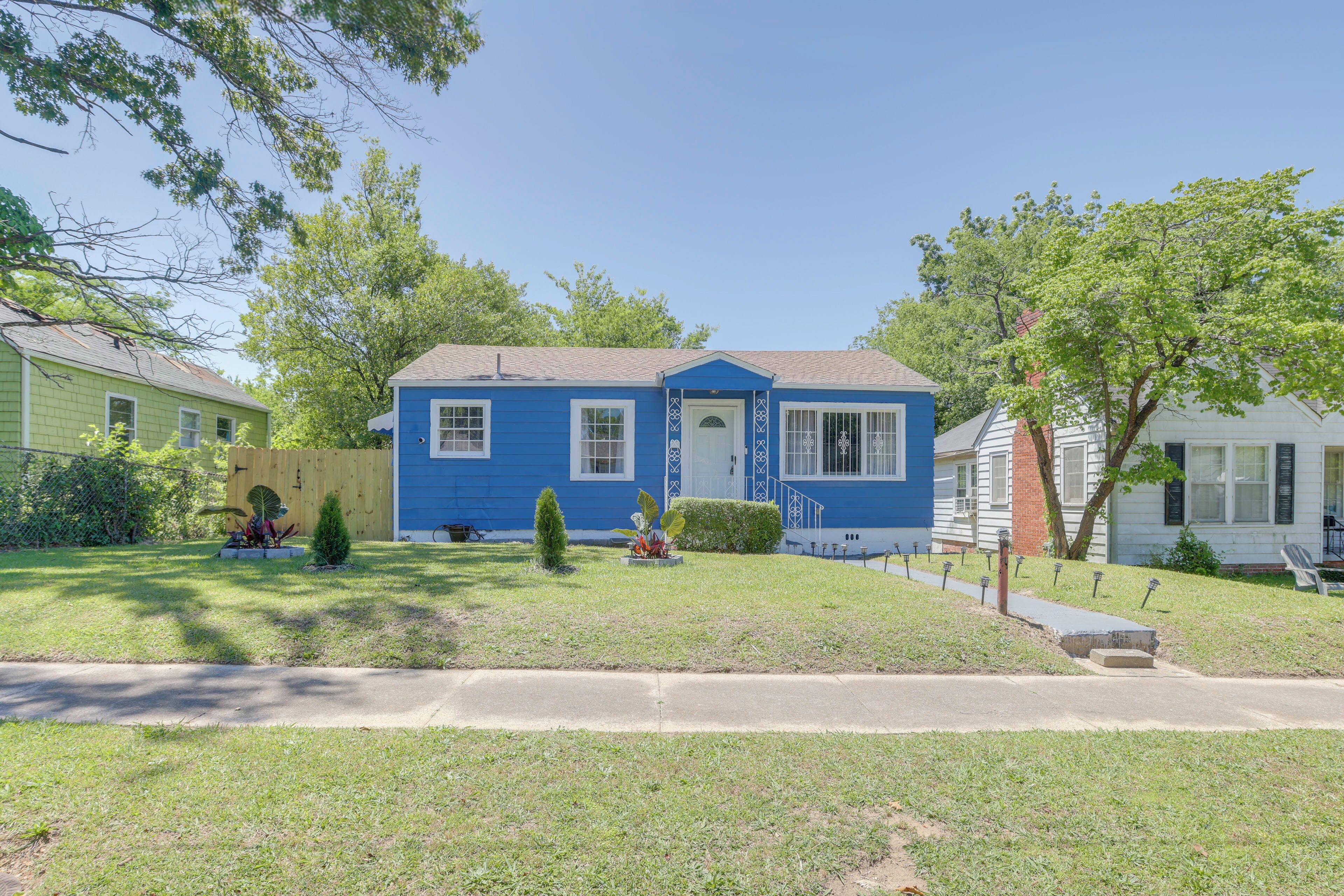 A residential house with a blue exterior, a front yard with a small tree and a decorative planter, and a sidewalk in front.