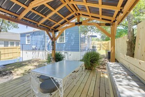 A covered outdoor patio with a table and chairs, surrounded by wooden fences and vegetation.