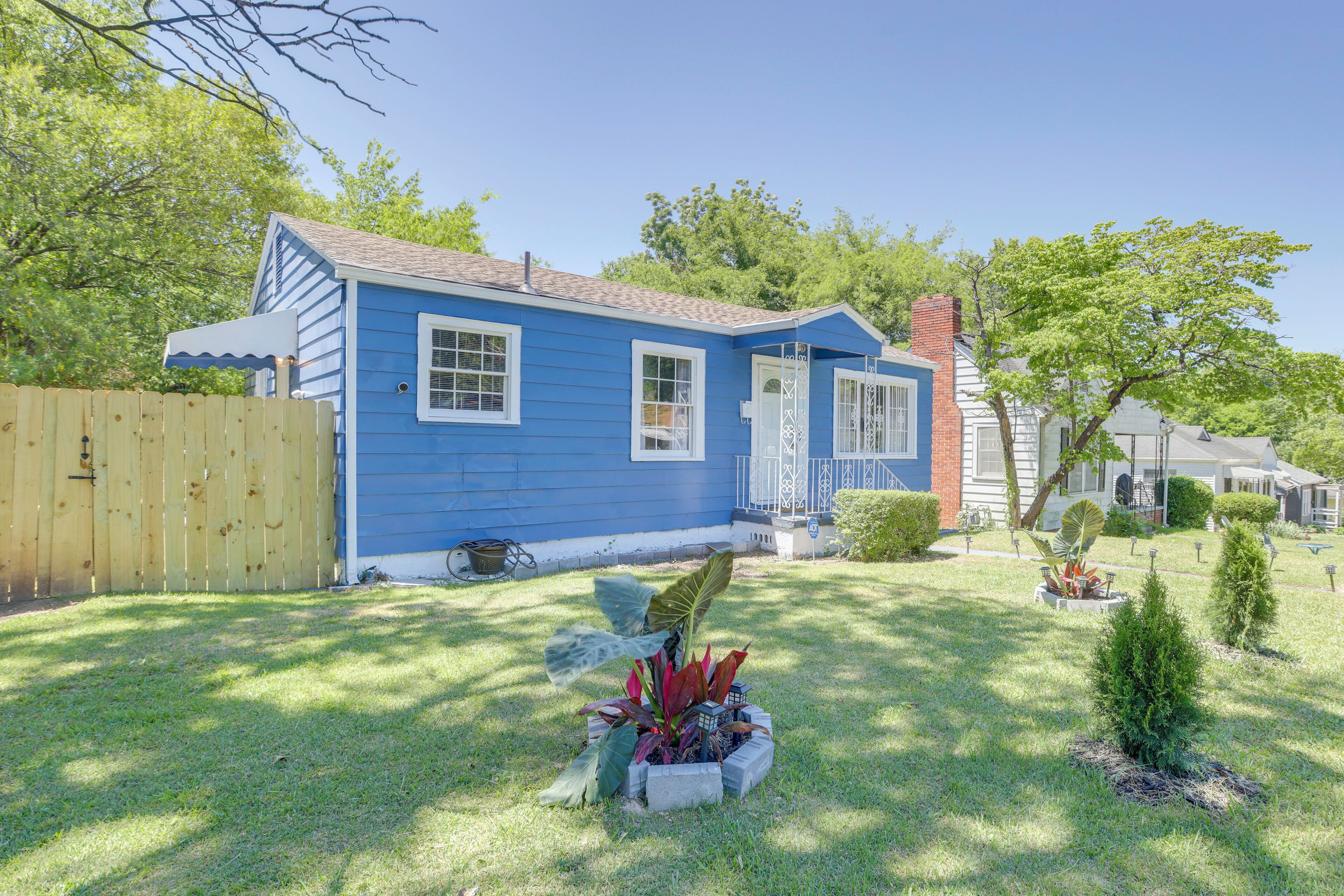 Una casa azul con patio cercado, un jardín pequeño y cielo despejado.